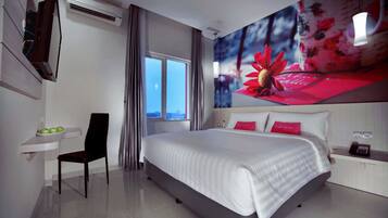 A modern hotel room with a large bed, a desk with a chair, a small table with apples, and a window with curtains.