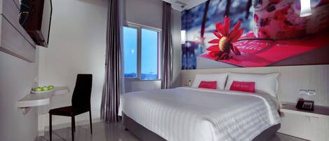 A modern hotel room with a large bed, a desk with a chair, a small table with apples, and a window with curtains.