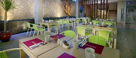 A modern dining area with multiple tables and chairs, a stone wall, and a staircase.