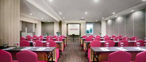 A conference room with rows of tables and chairs, a projector screen, and a presentation area.