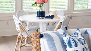 A cozy room with a white sofa, blue and white patterned pillows, a wicker pouf, and a dining area with wicker chairs and a white table. - The Wauwinet (Nantucket)