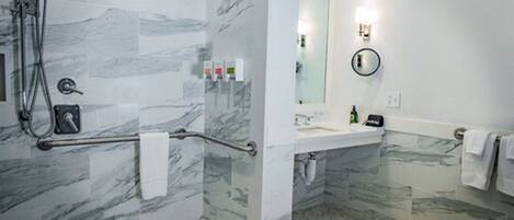 A modern bathroom with a shower, grab bar, and a large mirror.