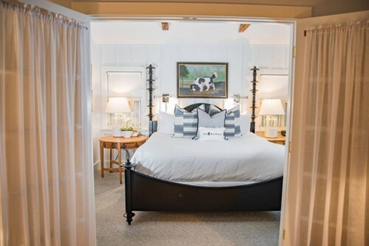 Une chambre à coucher avec un lit, deux tables de chevet, une lampe, un tableau au mur et une fenêtre avec des rideaux.