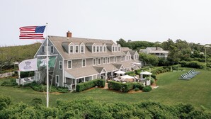 A large, multi-story building with a prominent American flag, a flag with a fleur-de-lis, and a sign indicating a restaurant. - The Wauwinet (Nantucket)