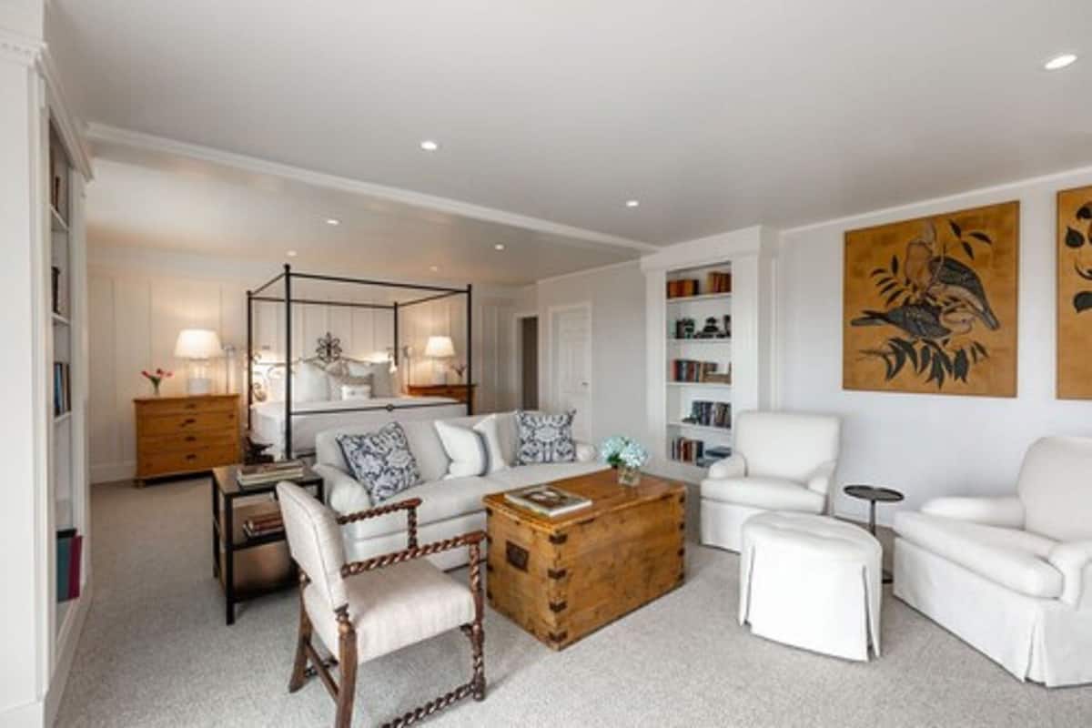 Un salon moderne avec un canapé blanc, une table basse en bois et un fauteuil blanc. On y trouve une bibliothèque et un tableau décoratif représentant un oiseau, accroché au mur.