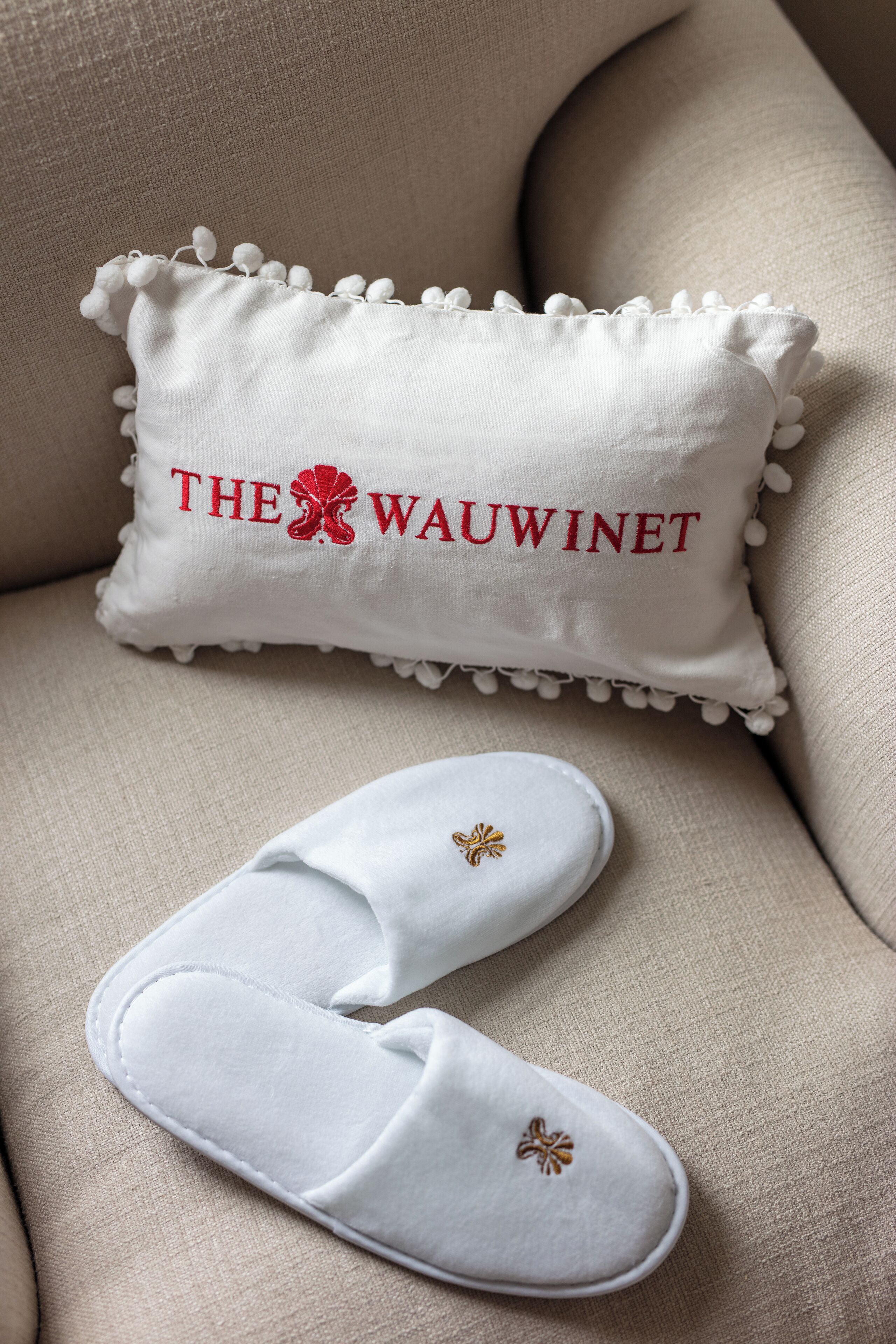 A beige sofa with a white pillow featuring embroidered text and a small embroidered flower.