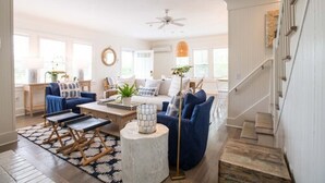 A spacious living room with a blue sofa, a coffee table, and a staircase leading to an upper floor. - The Wauwinet (Nantucket)