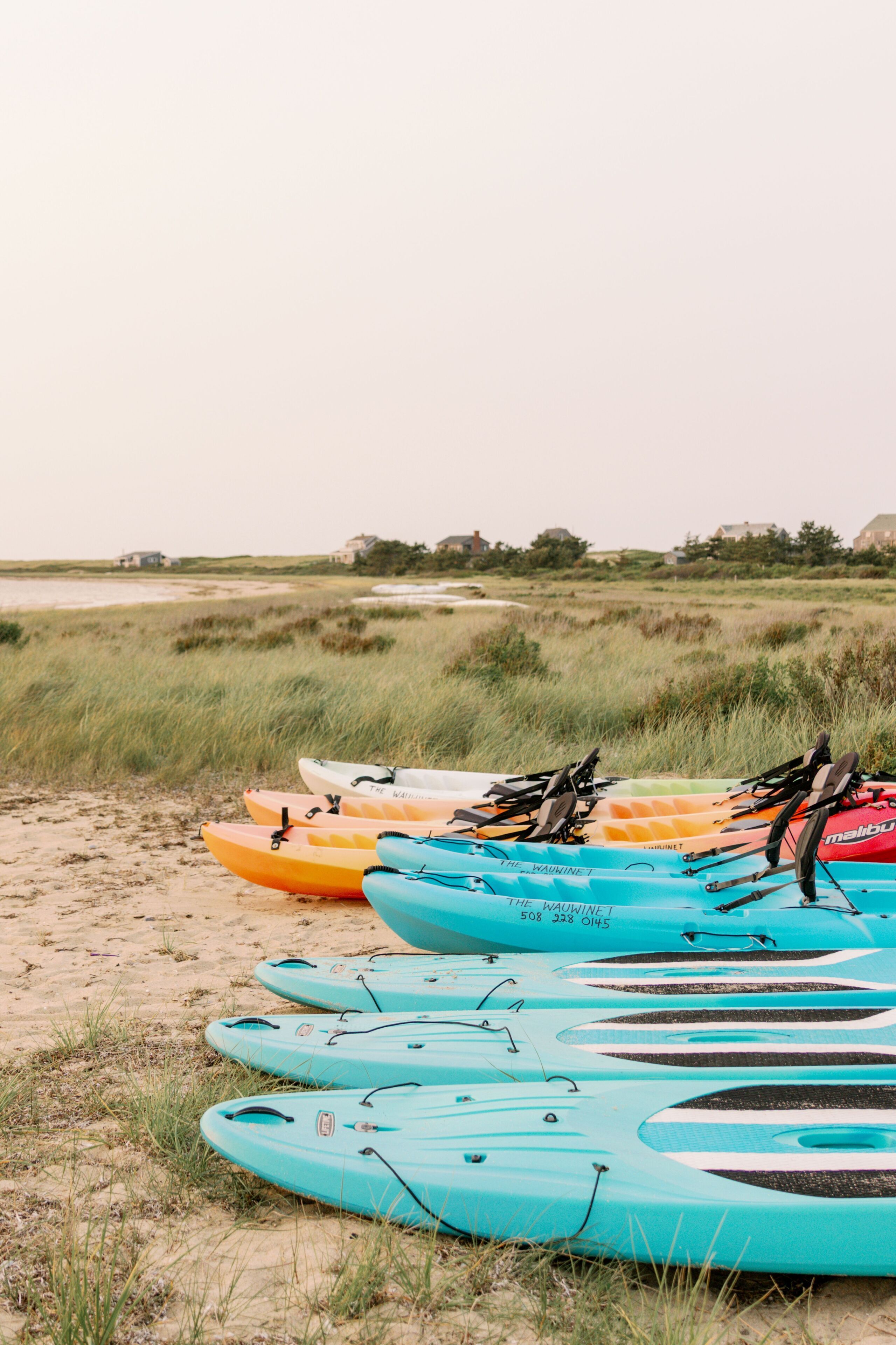 Kayaks alineados en una playa arenosa con hierba al fondo.