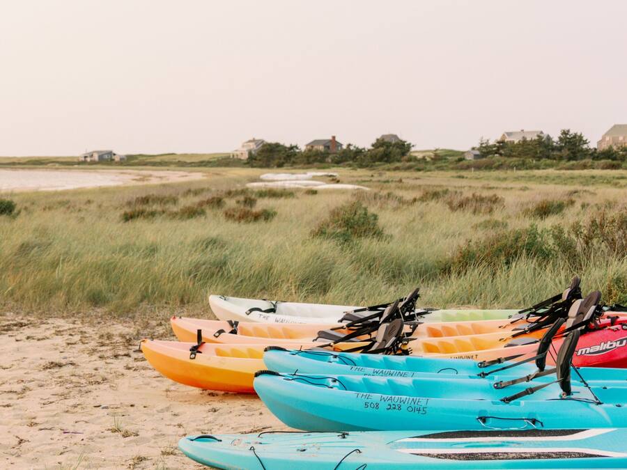 Kayaks lined up on a sandy beach with grass in the background.