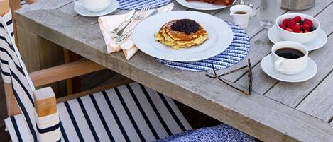 A wooden dining table set with plates of food, cups, and a pitcher.