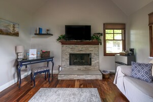 A living room with a fireplace, a television mounted above it, a sofa, a coffee table, and a bookshelf.