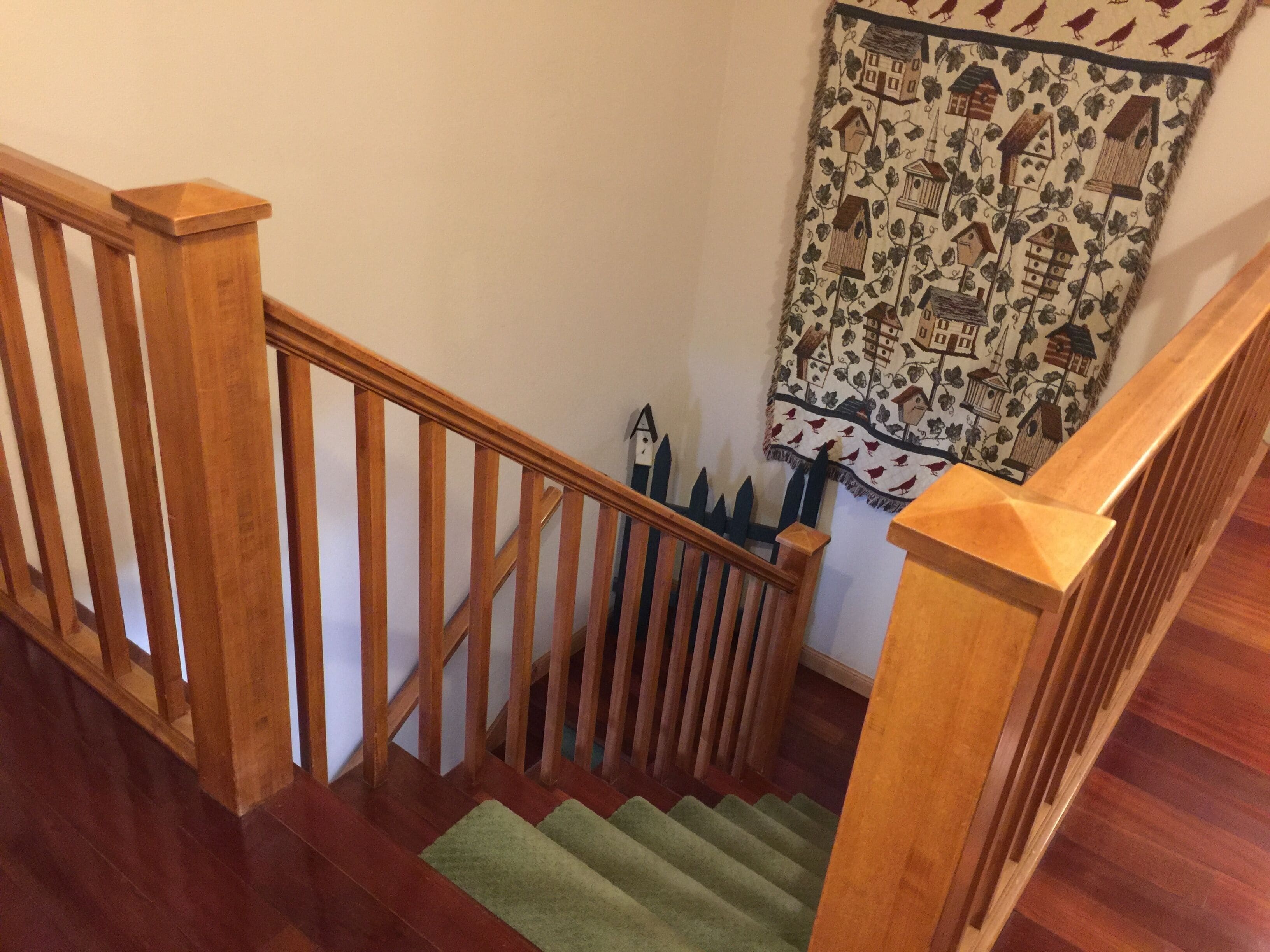 A wooden staircase with a green carpet, a wooden handrail, and a wall with a birdhouse pattern.