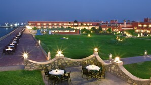 A waterfront hotel with outdoor dining areas, stone walls, and a well-lit lawn. - Helnan Auberge Hotel (Sinnuris)