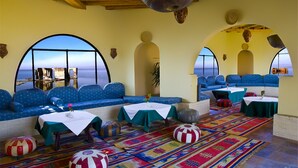 A room with a view of the sea, blue upholstered seating, tables with white tablecloths, and colorful rugs. - Helnan Auberge Hotel (Sinnuris)
