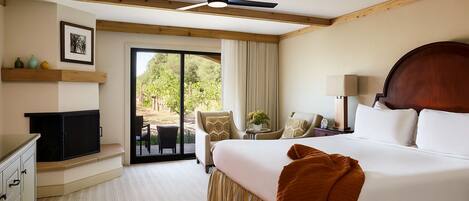 Habitación de hotel con una cama grande, ventilador de techo, televisión, escritorio y vistas al exterior.