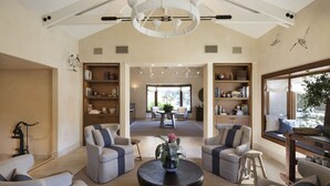 A spacious living room with a high ceiling, a central coffee table, and two seating areas with bookshelves. - Napa Valley Lodge (Yountville)