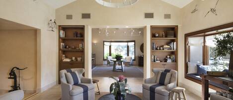 A spacious living room with a high ceiling, a central coffee table, and two seating areas with bookshelves.