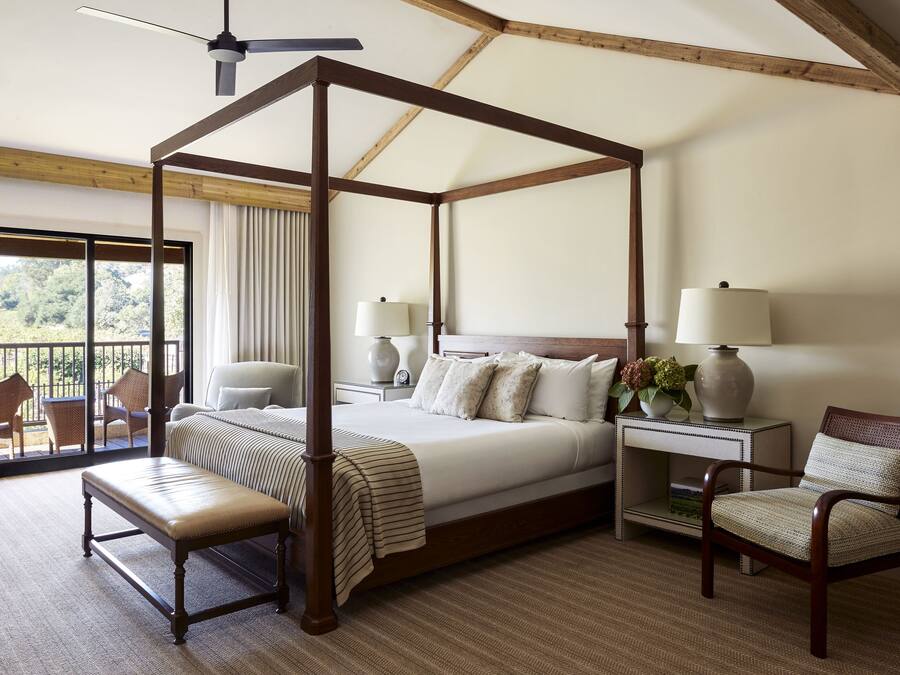 A four-poster bed with a ceiling fan, a bench, a chair, and a nightstand with lamps.