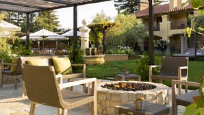 An outdoor patio area with wicker furniture, a stone fire pit, and a pergola structure. - Napa Valley Lodge (Yountville)
