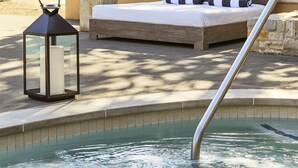 A spa area with a hot tub, a lounge chair, and a bed with a view of the building in the background. - Napa Valley Lodge (Yountville)