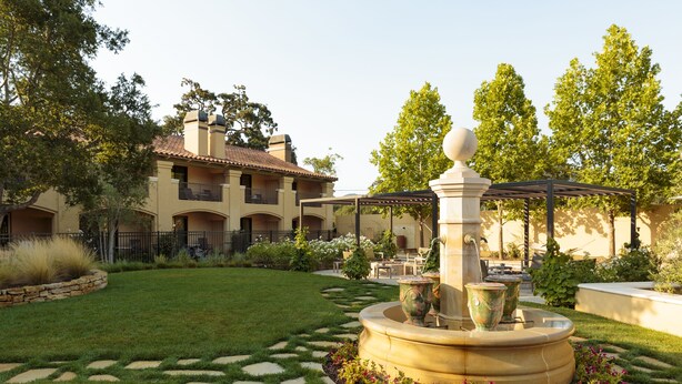 A courtyard with a fountain, a pergola, and a building with multiple balconies. - Napa Valley Lodge (Yountville)