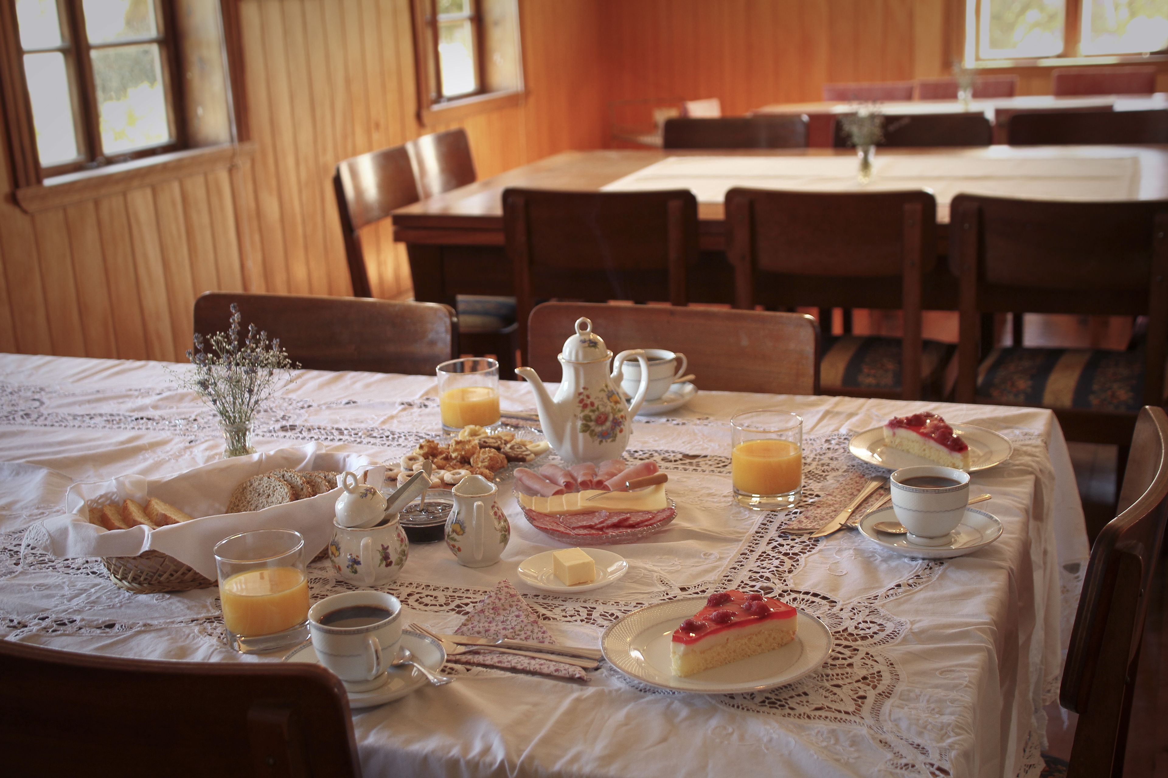 A breakfast setting with a table set for two, including plates of food, cups, and a teapot.
