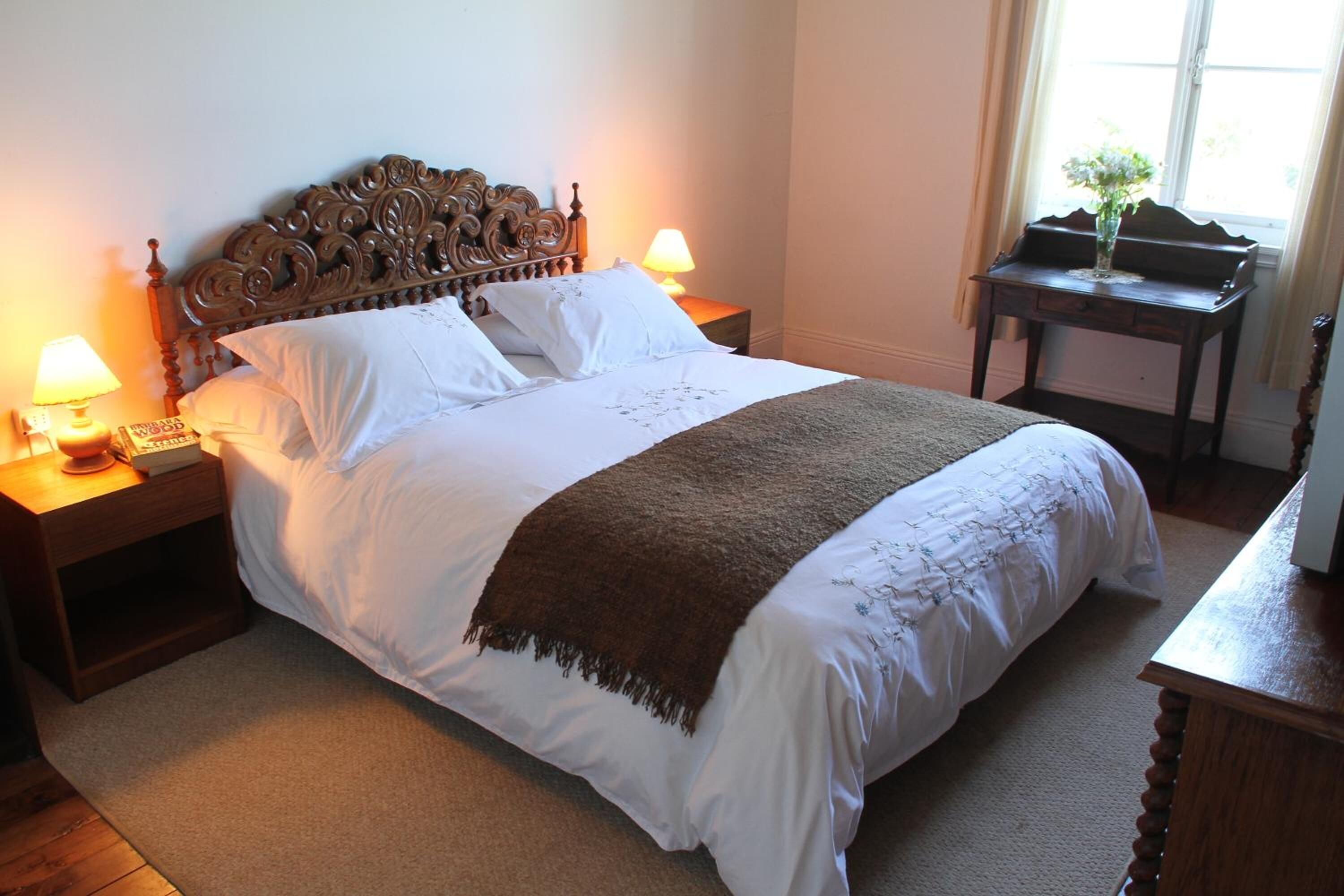 A neatly made bed with a wooden headboard, two bedside lamps, and a small table with a vase of flowers.
