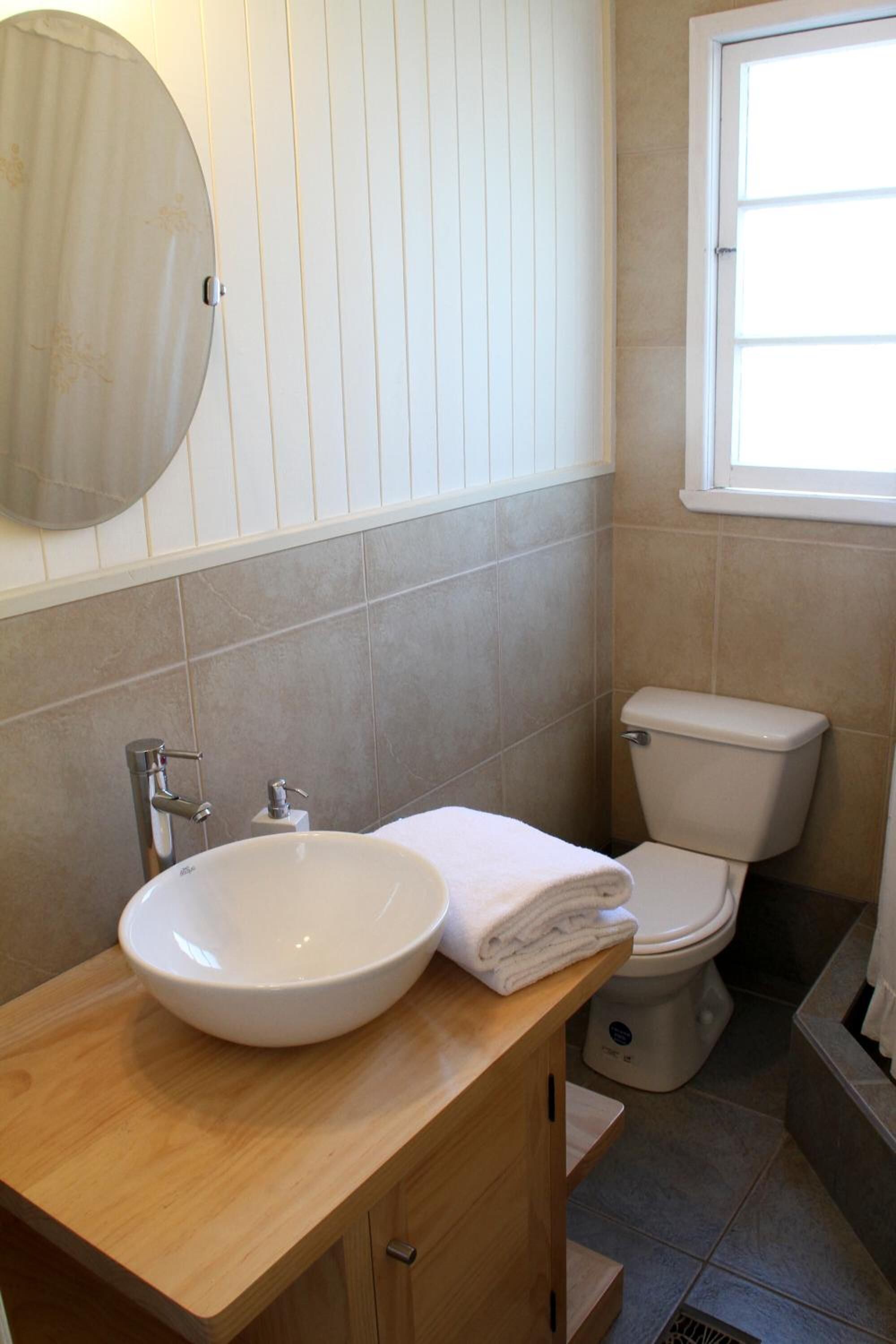 A bathroom with a wooden vanity, a white sink, a toilet, and a window.