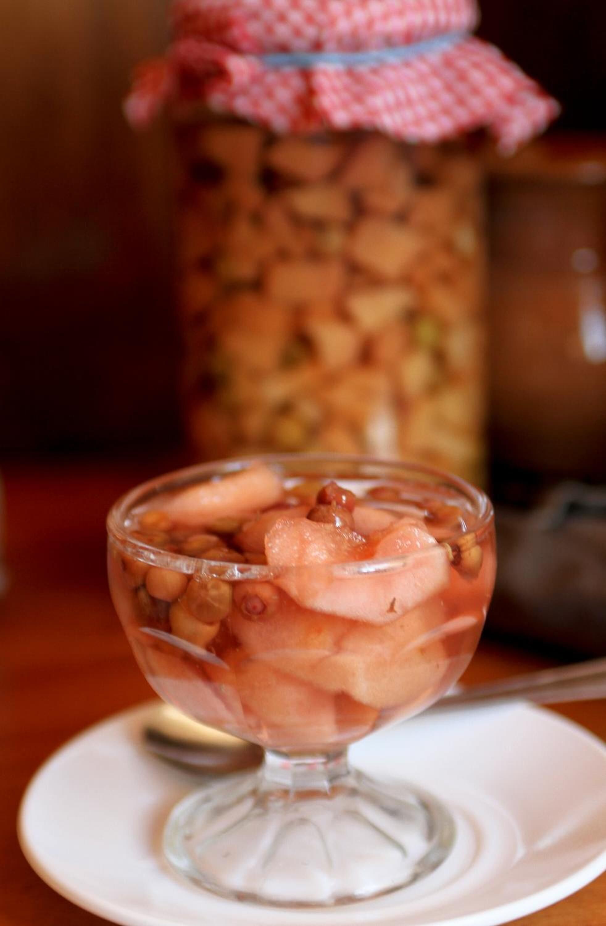 A dessert in a glass bowl on a white plate, with a jar of nuts in the background.