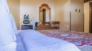 A hotel room with a bed, a wooden chair, a small table with a microwave and a coffee maker, and a mirror on the wall.