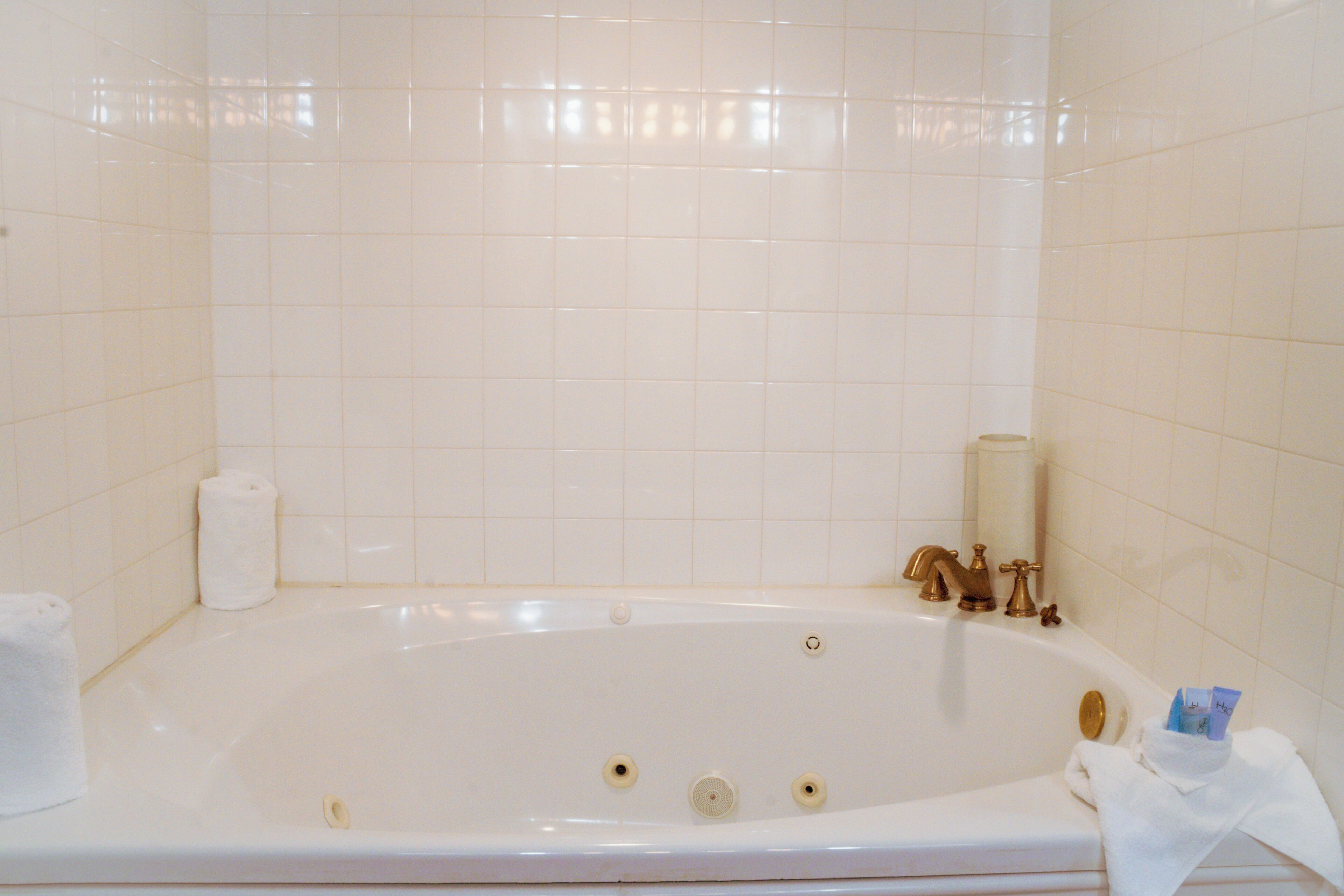 Una bañera blanca con dos grifos, un rollo de papel higiénico y una toalla al lado.