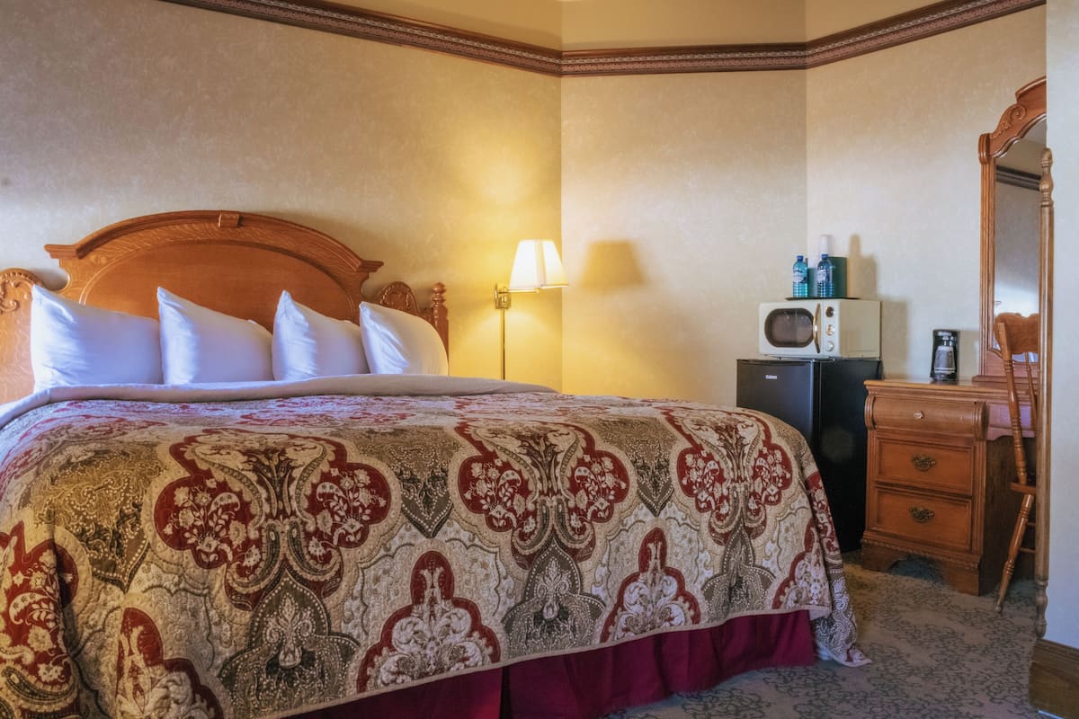 A hotel room with a large bed, a nightstand, a lamp, a microwave, and a dresser.