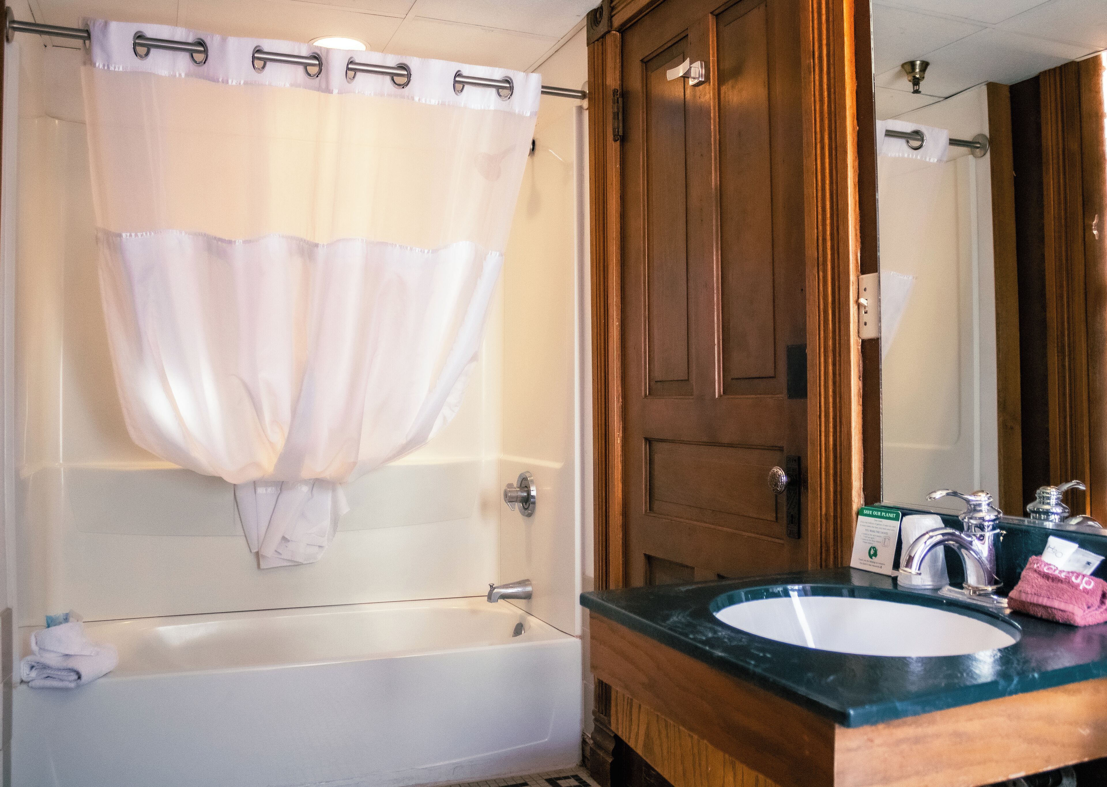 A bathroom with a bathtub, a shower curtain, a wooden door, a sink with a mirror, and a towel rack.