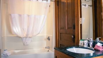 A bathroom with a bathtub, a shower curtain, a wooden door, a sink with a mirror, and a towel rack.