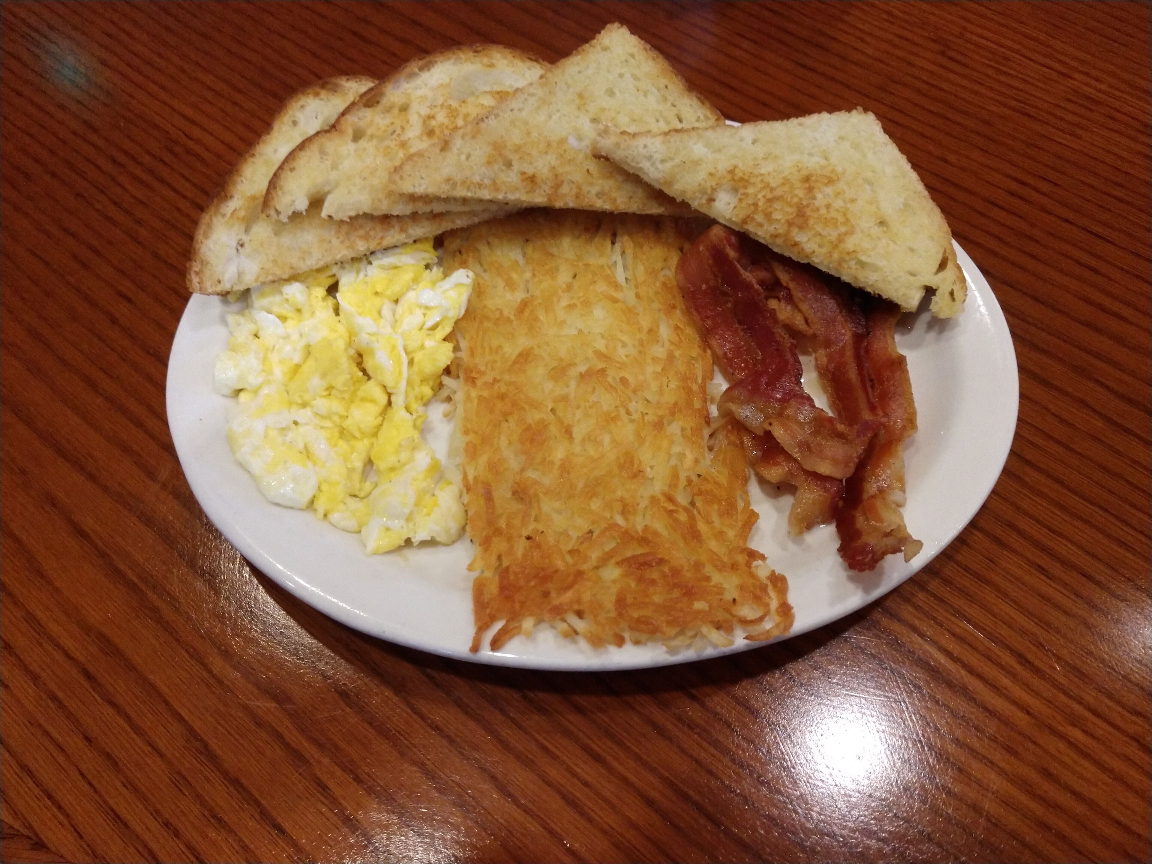 Un plato con huevos revueltos, patatas ralladas, tocino y pan tostado.