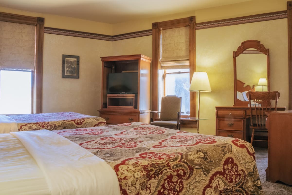A hotel room with two beds, a television, a desk with a chair, a lamp, and a mirror.