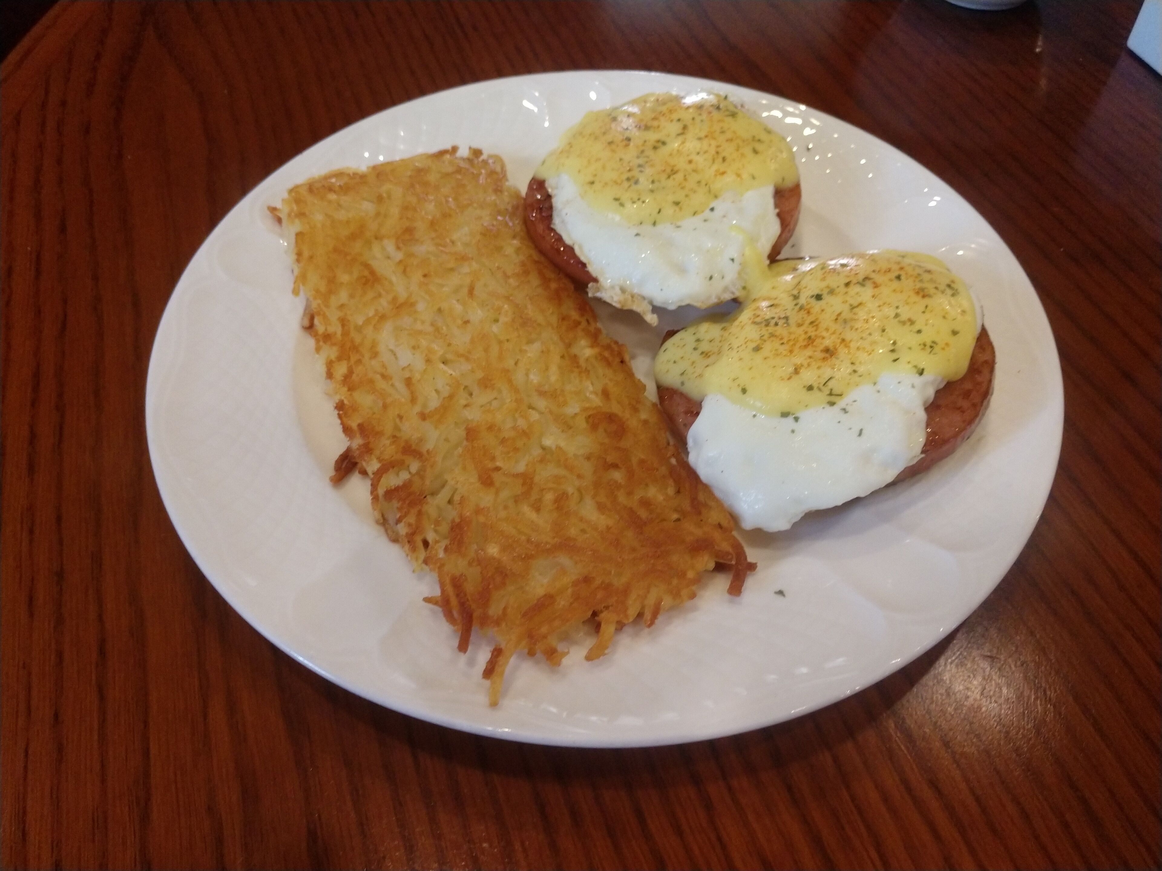 A plate with two eggs benedict sandwiches and a hash brown.