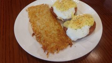 A plate with two eggs benedict sandwiches and a hash brown.