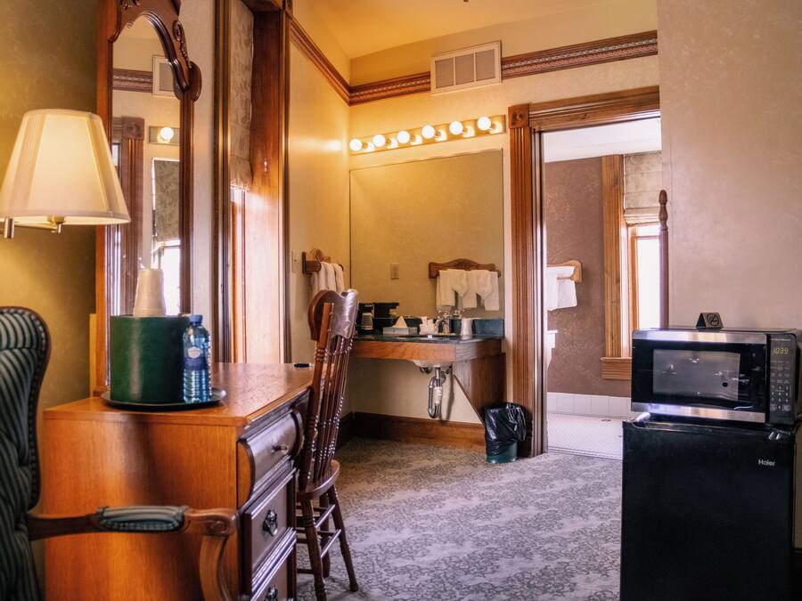 A hotel bathroom with a vanity, a mirror, a sink, a microwave, and a chair.