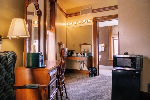 A hotel bathroom with a vanity, a mirror, a sink, a microwave, and a chair.