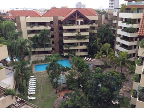 A multi-story hotel with a swimming pool surrounded by palm trees and lounge chairs. - Apart Hotel Toborochi (Santa Cruz)