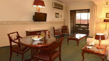 A hotel room with a dining table, chairs, a TV, a sofa, and a balcony with a view.