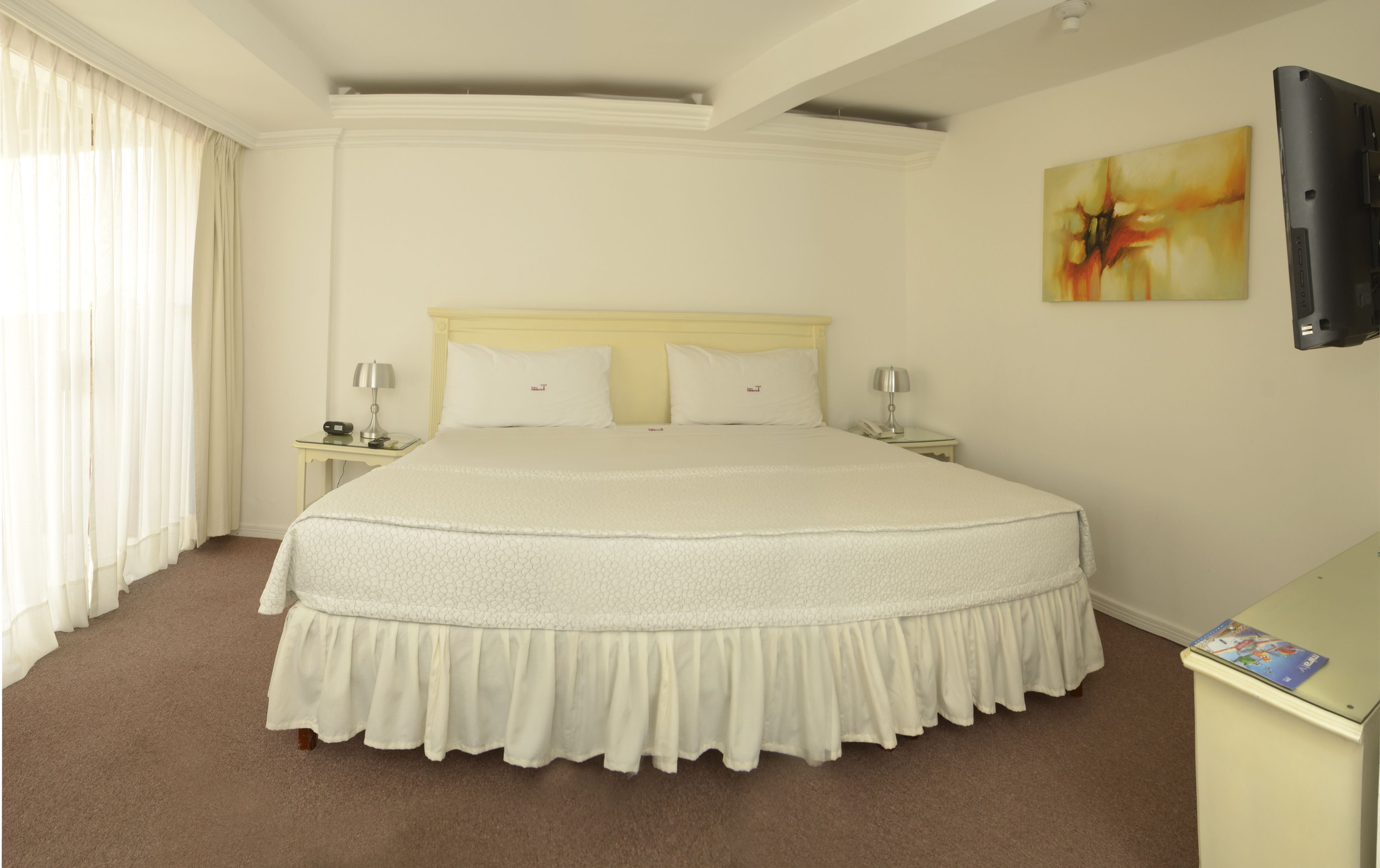 A hotel room with a large bed, two bedside tables, a flat-screen TV, and a painting on the wall.