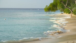 A beach scene with two children playing in the sand, a clear sky, and calm sea waves. - Coral Lane Beach Apartments (Paynes Bay)
