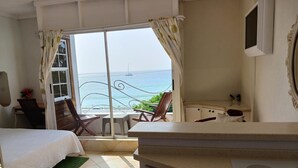 A bedroom with a bed, a desk, a chair, and a view of the sea. - Coral Lane Beach Apartments (Paynes Bay)