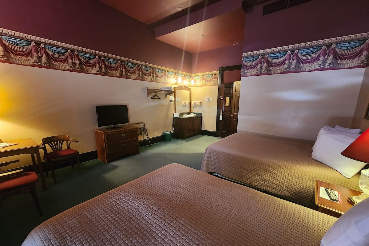 A hotel room with two beds, a desk with a chair, a television, a dresser, and a door.