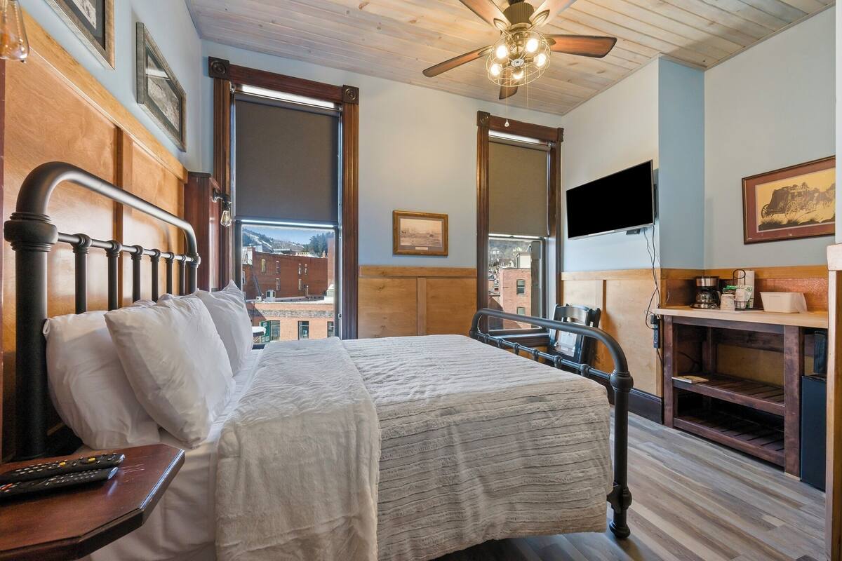 A hotel room with a bed, a desk with a lamp, a TV, and a ceiling fan.