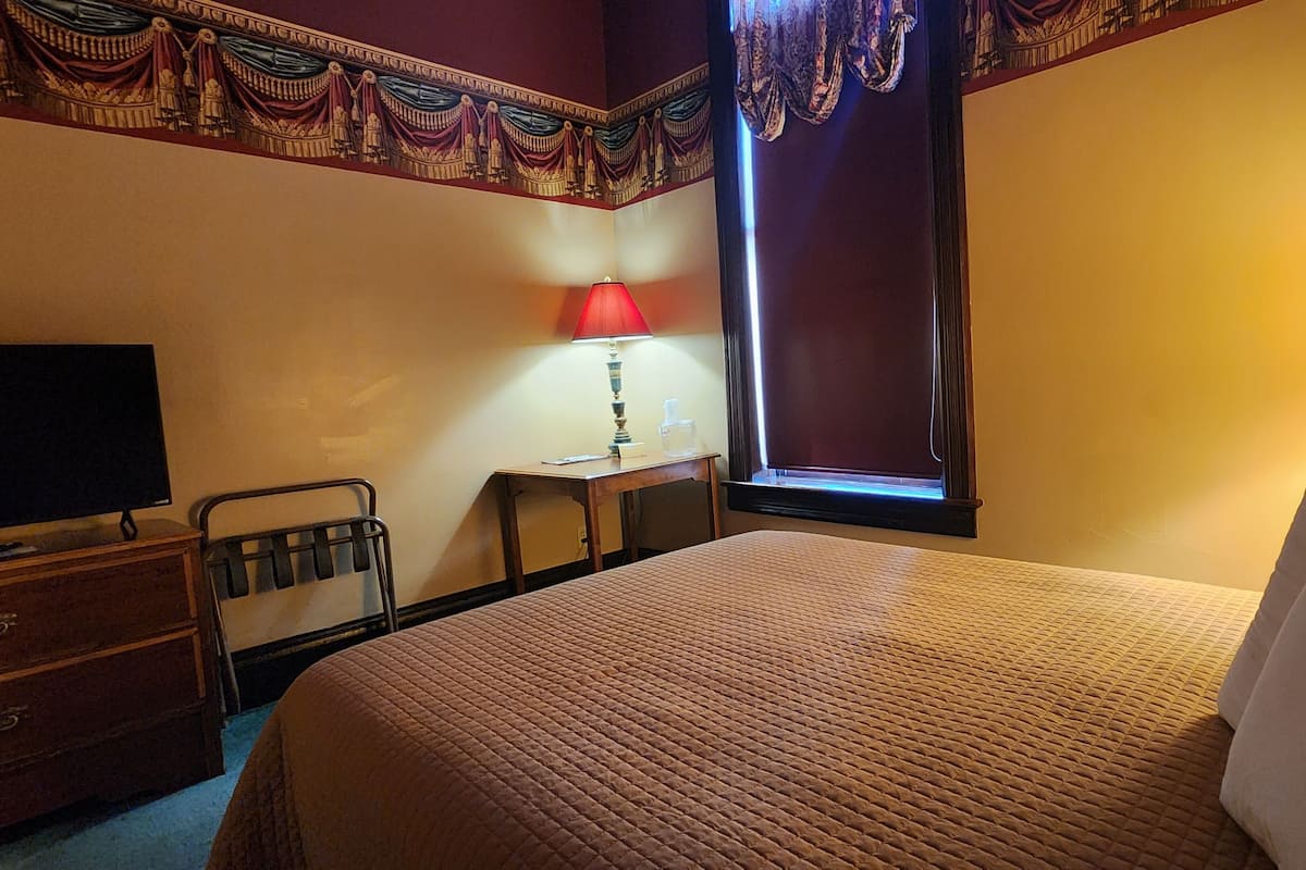 A hotel room with a bed, a desk, a chair, a TV, and a window with curtains.