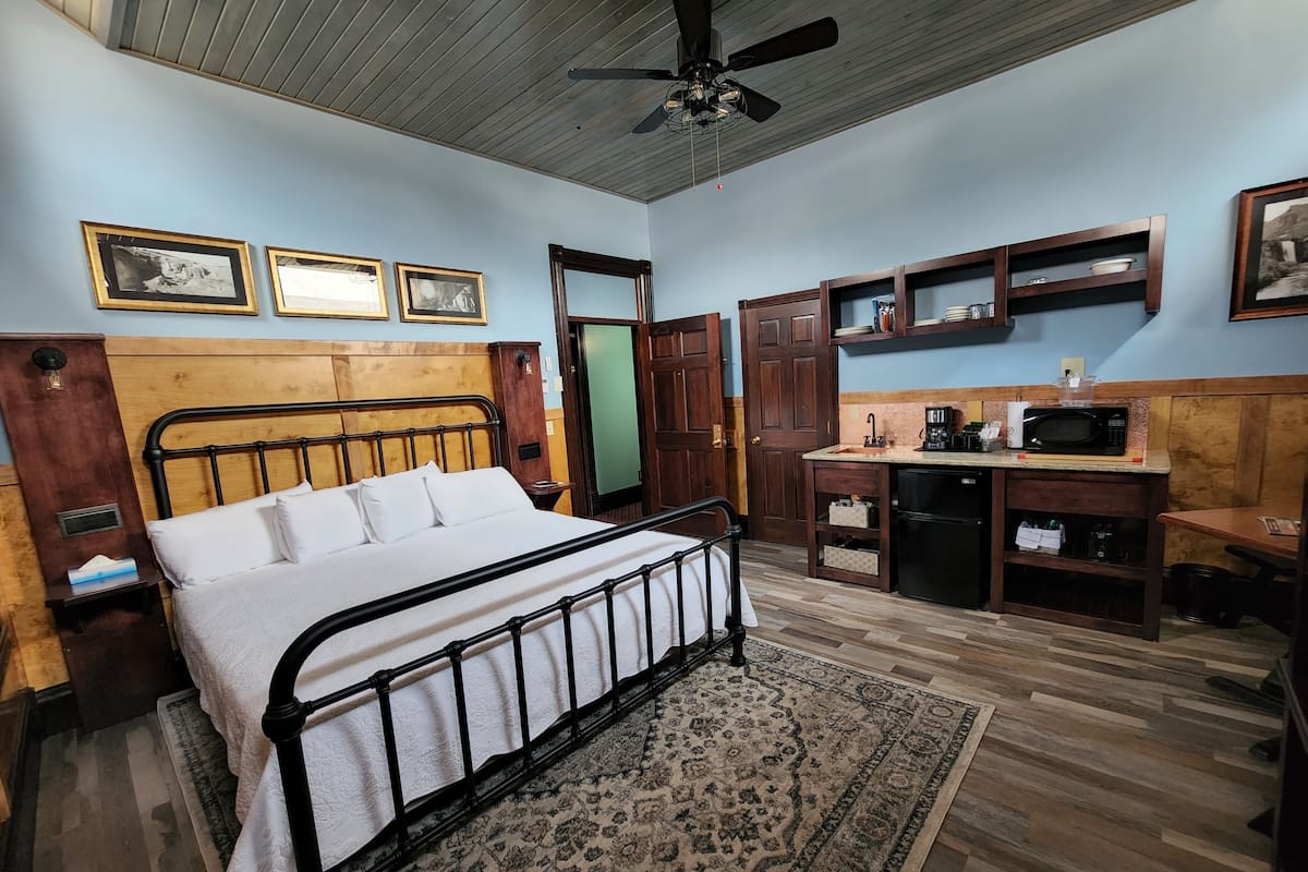 A bedroom with a bed, a desk, a microwave, and a sink.