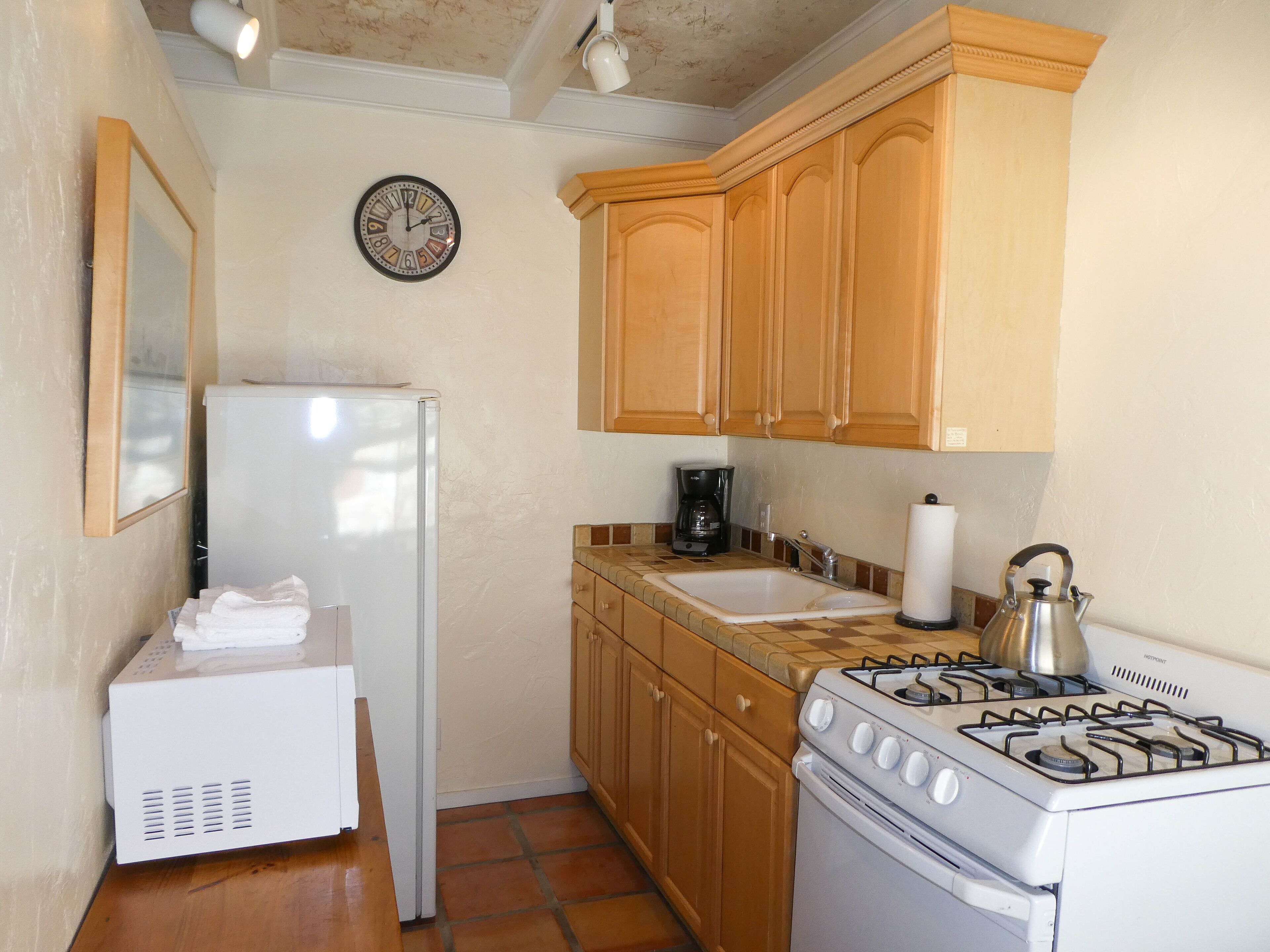 Una cocina compacta con armarios de madera, un refrigerador blanco, una estufa a gas y una cafetera.